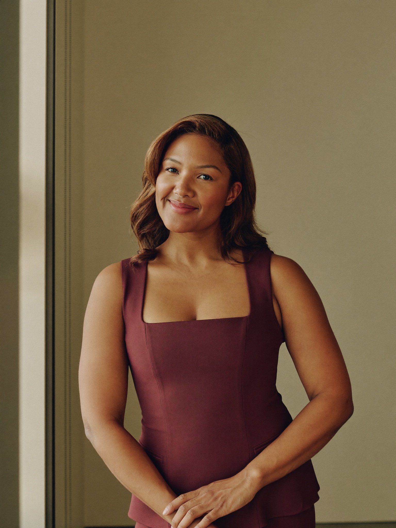 A calm, confident woman in a fitted sleeveless top, at ease in warm natural light