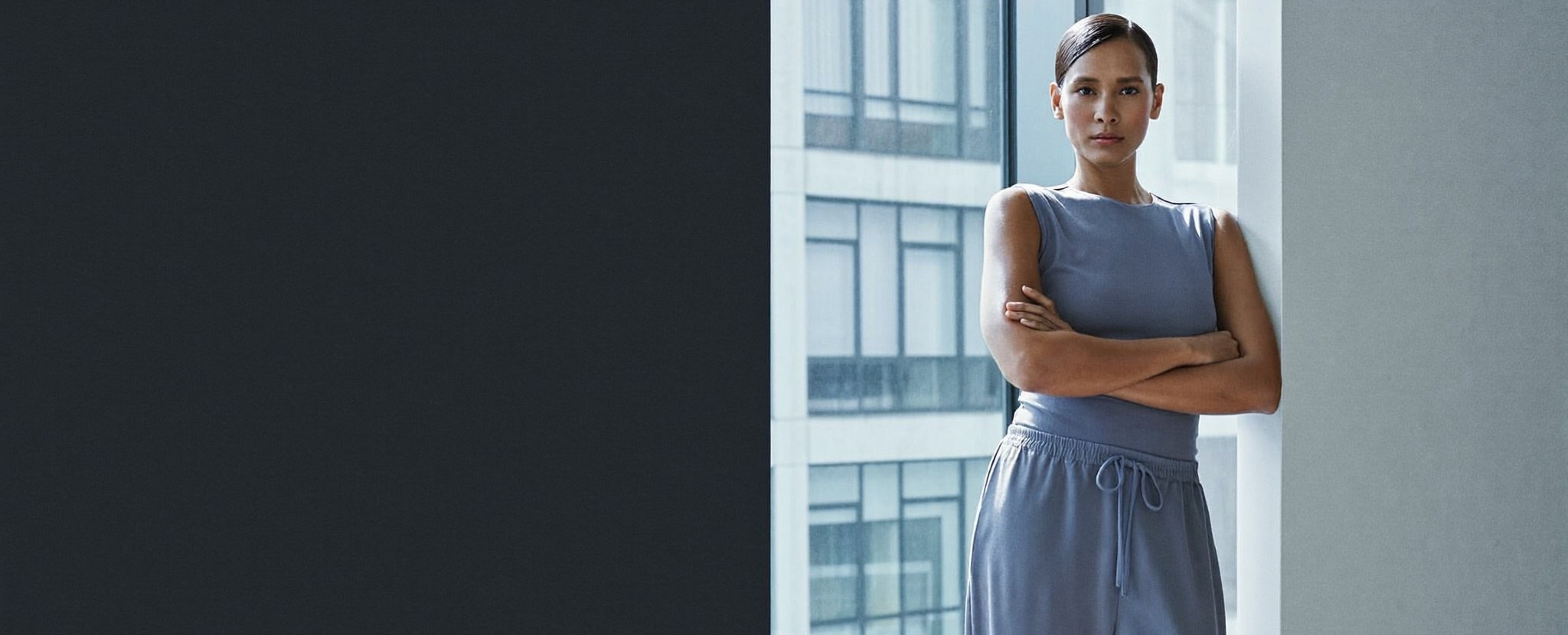 A poised, confident adult in a fitted sleeveless top at ease by a window in a modern interior